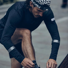 Load image into Gallery viewer, Runner wearing black Bookman reflective slap wraps around the lower legs while adjusting running gear outdoors.
